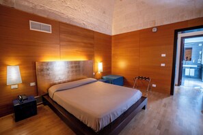 Habitación de hotel con una cama grande, paredes de madera, una mesita de noche con teléfono y una pequeña mesa con lámpara.