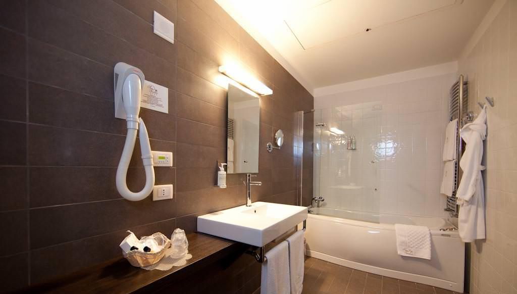 Un baño moderno con un espejo grande, un lavamanos blanco, una ducha con mampara de cristal y un perchero para toallas.
