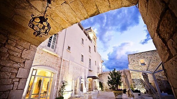 Un edificio de piedra con un patio, sillas y mesas blancas.