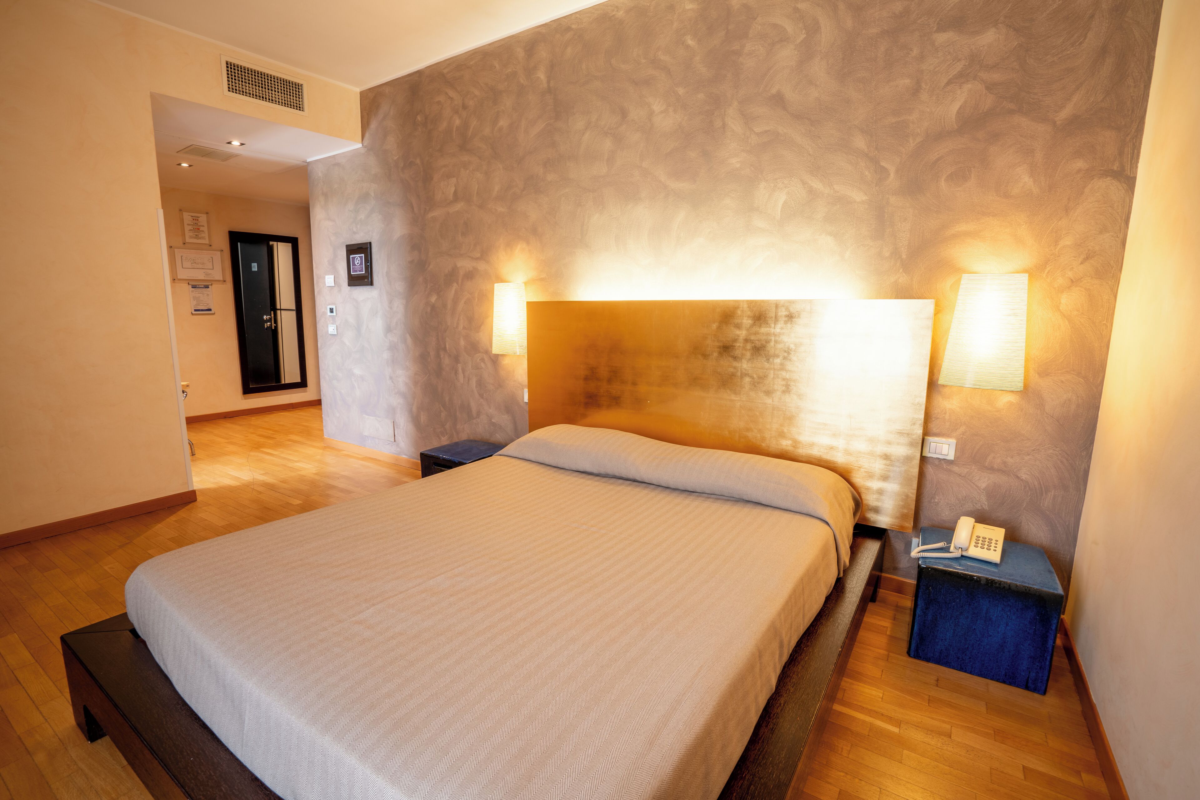 Een hotelkamer met een groot bed, twee bedlampen, een telefoon op het nachtkastje en een klein tafeltje.