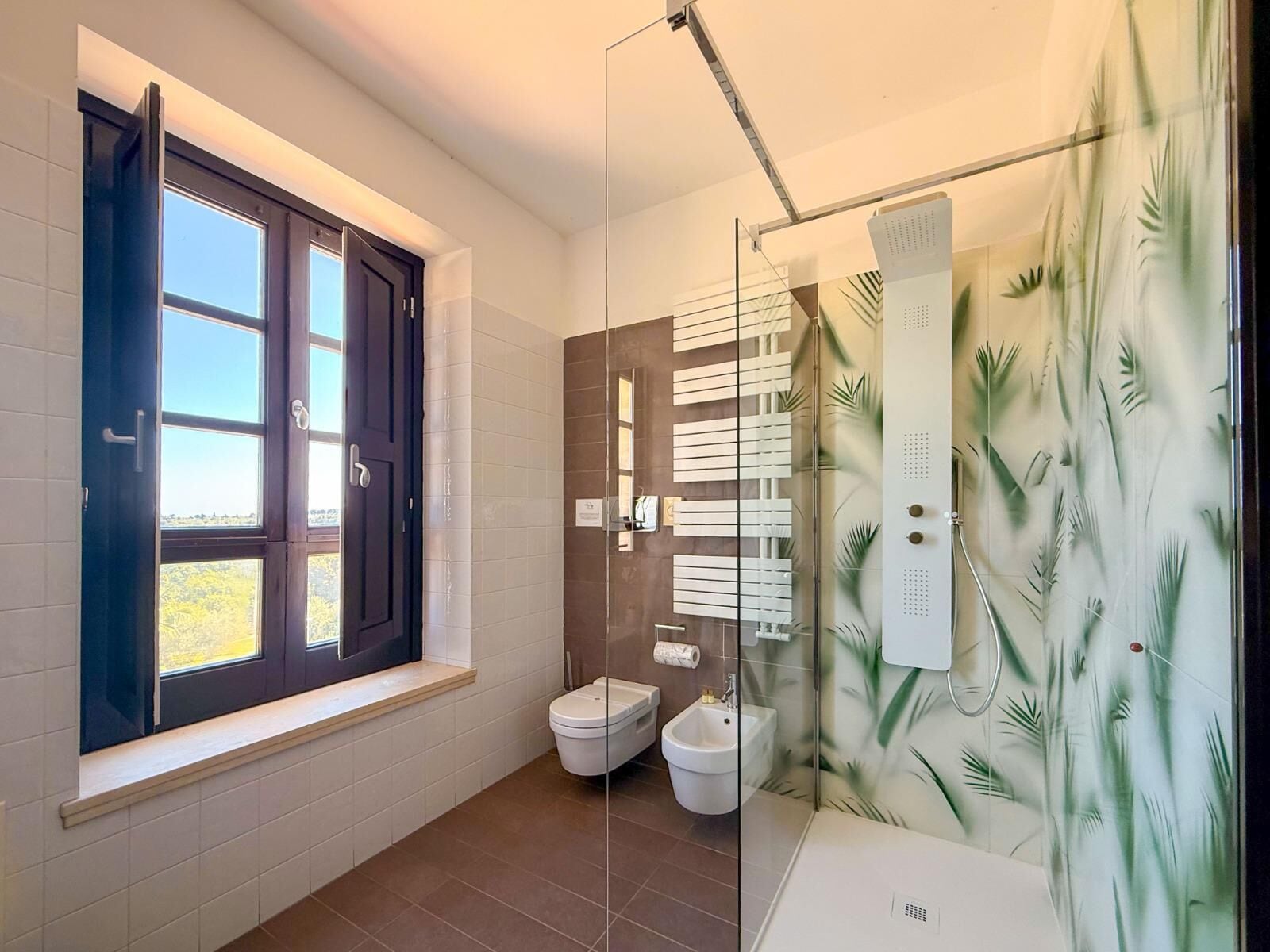 Un baño moderno con ventana, inodoro, bidé y ducha con puerta de vidrio.