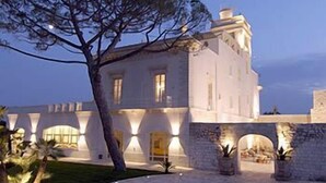 Un edificio grande y blanco con varios arcos y un árbol destacado en primer plano.