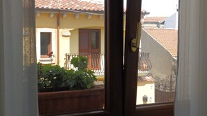 A view through a window of a building with a tiled roof, a balcony with a wooden railing, and a potted plant. - Sa Chessa (Ploaghe)