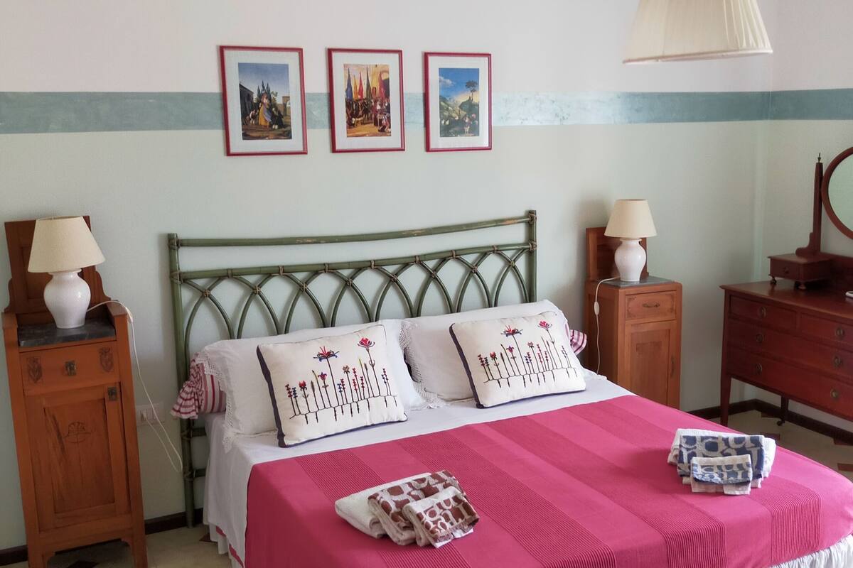 A neatly arranged bedroom with a bed, bedside tables, a dresser, a mirror, and wall-mounted pictures.