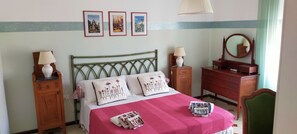 Une chambre à coucher bien rangée, avec un lit, des tables de chevet, une commode, un miroir et des tableaux accrochés au mur.