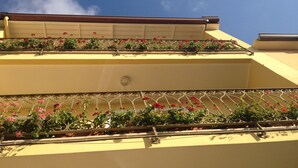 A building with a yellow facade and balconies adorned with red flowers. - Sa Chessa (Ploaghe)