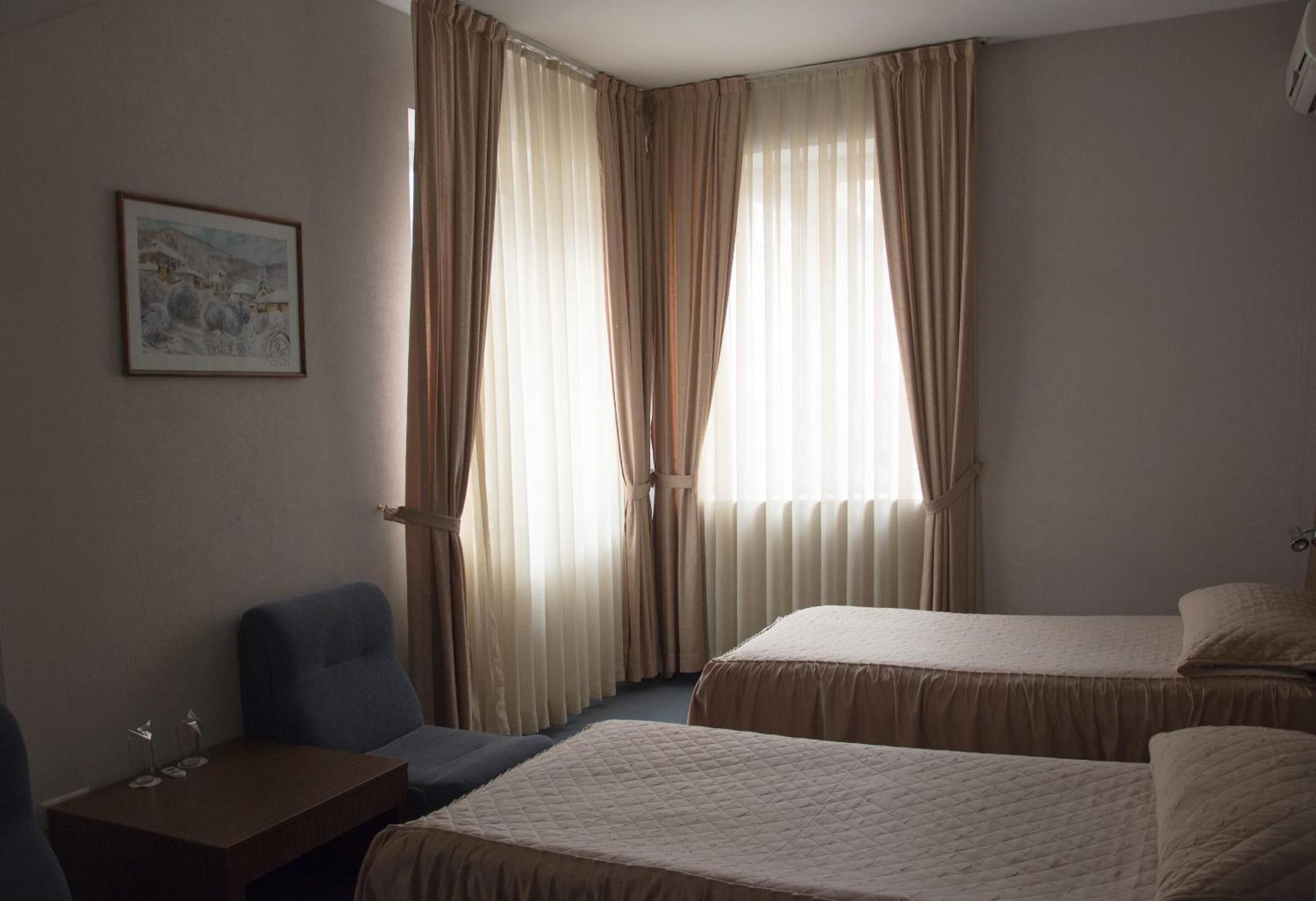 A hotel room with two beds, a desk, a chair, and a painting on the wall.