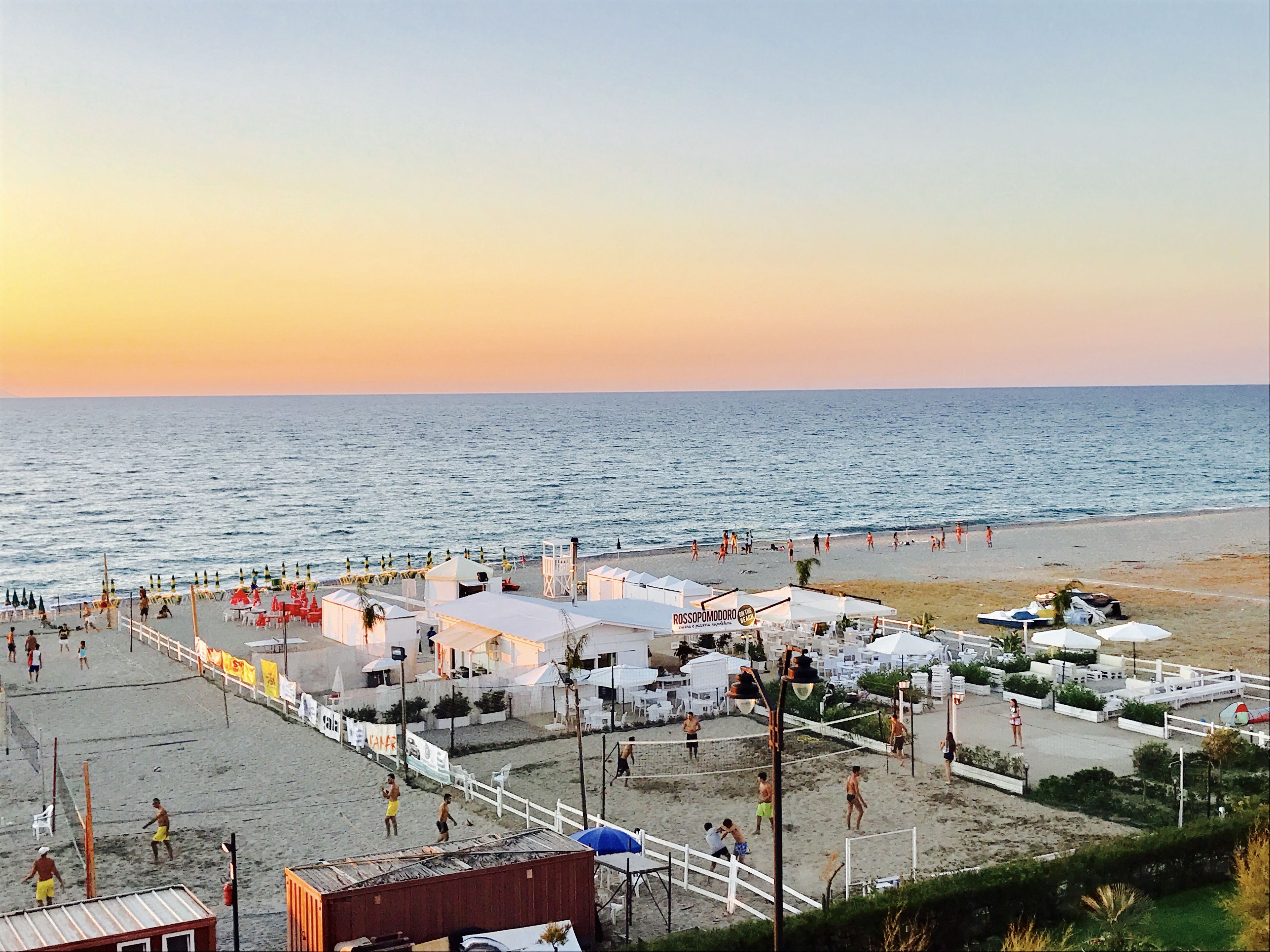 A beachside area with a volleyball court, umbrellas, and beach chairs.