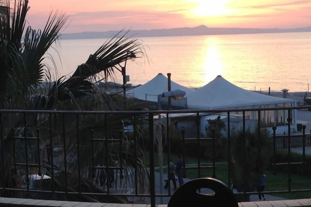 Ein Sonnenuntergangsblick von einer Terrasse mit Tisch und Stühlen, mit Blick auf ein Gewässer und einen Berg.