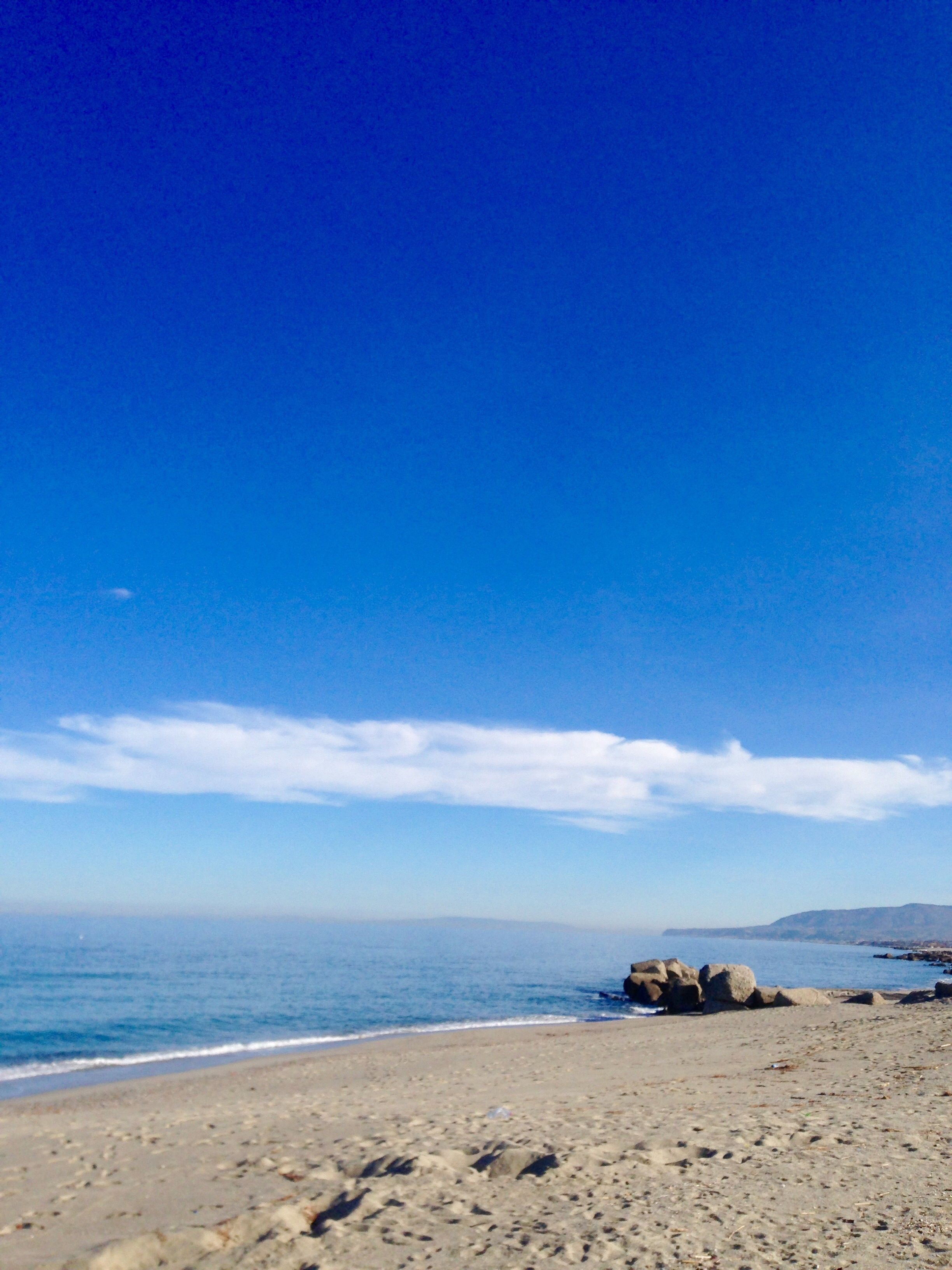 A beach with clear skies, calm water, and rocky outcrops.