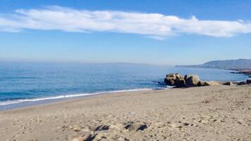 A beach with clear skies, calm water, and rocky outcrops.