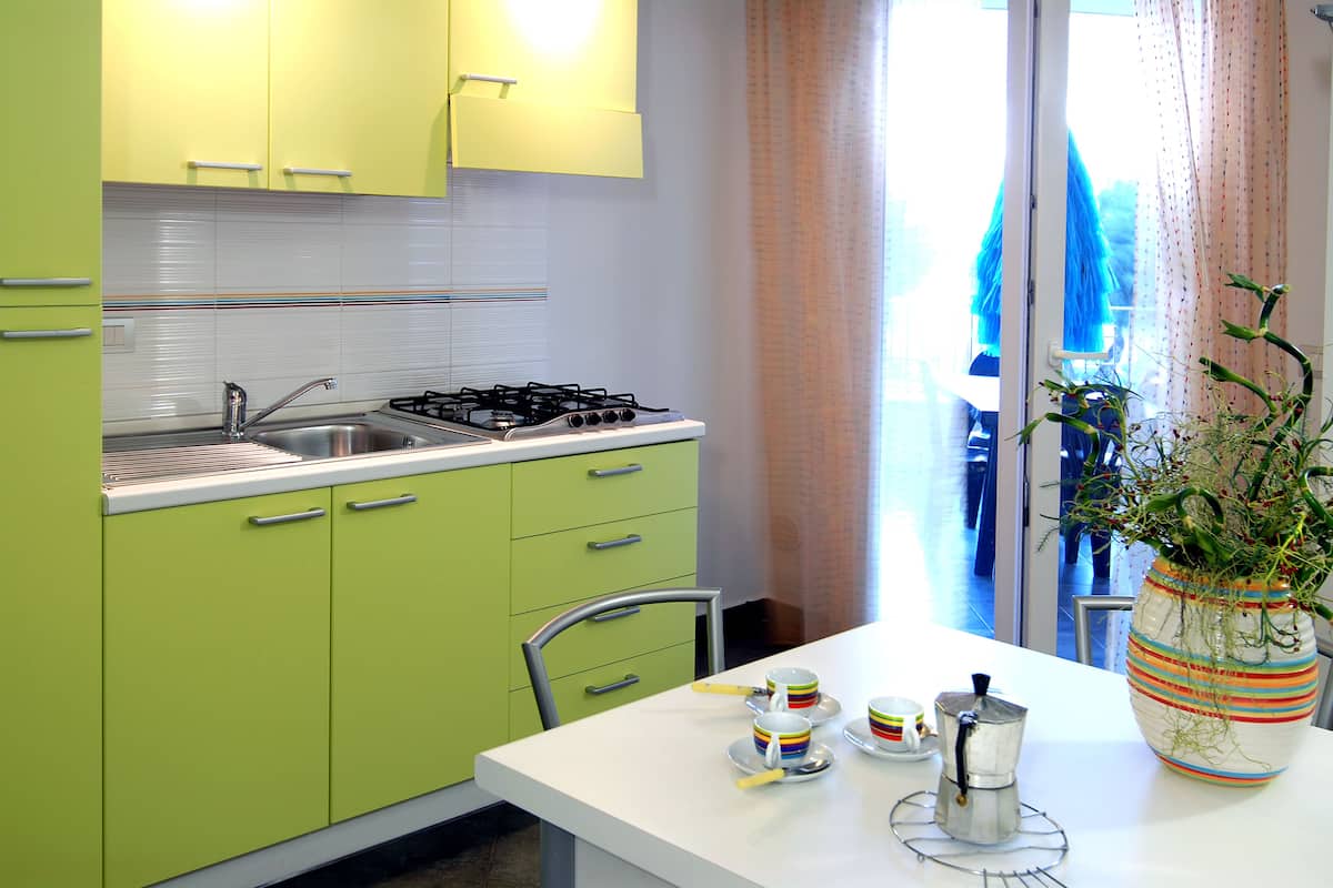 Eine Küche mit grünen Schränken, einer weißen Arbeitsplatte und einem Fenster mit Vorhängen.