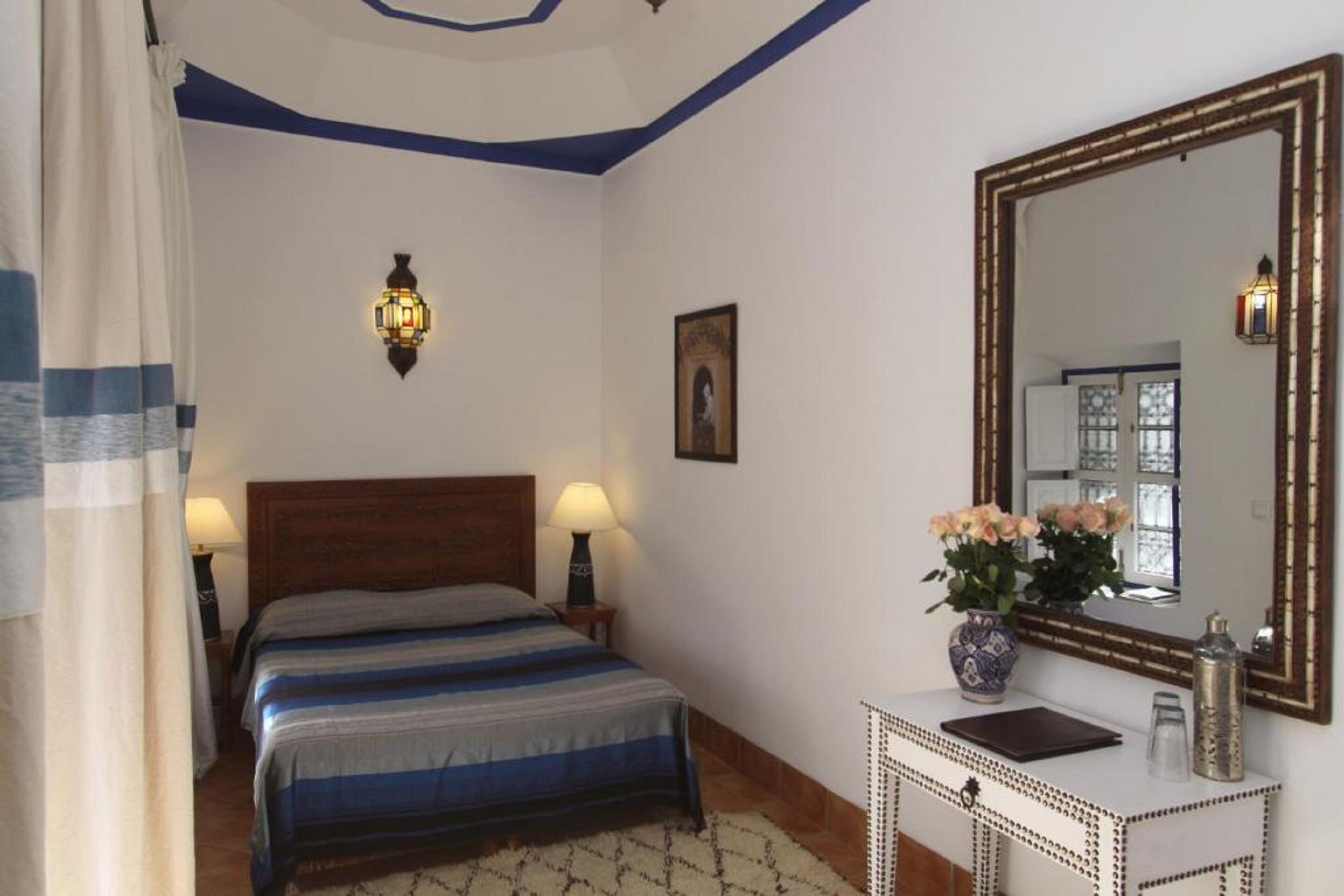 Un dormitorio con cama, lámparas de noche, mesita de noche, cómoda, espejo y un cuadro en la pared.
