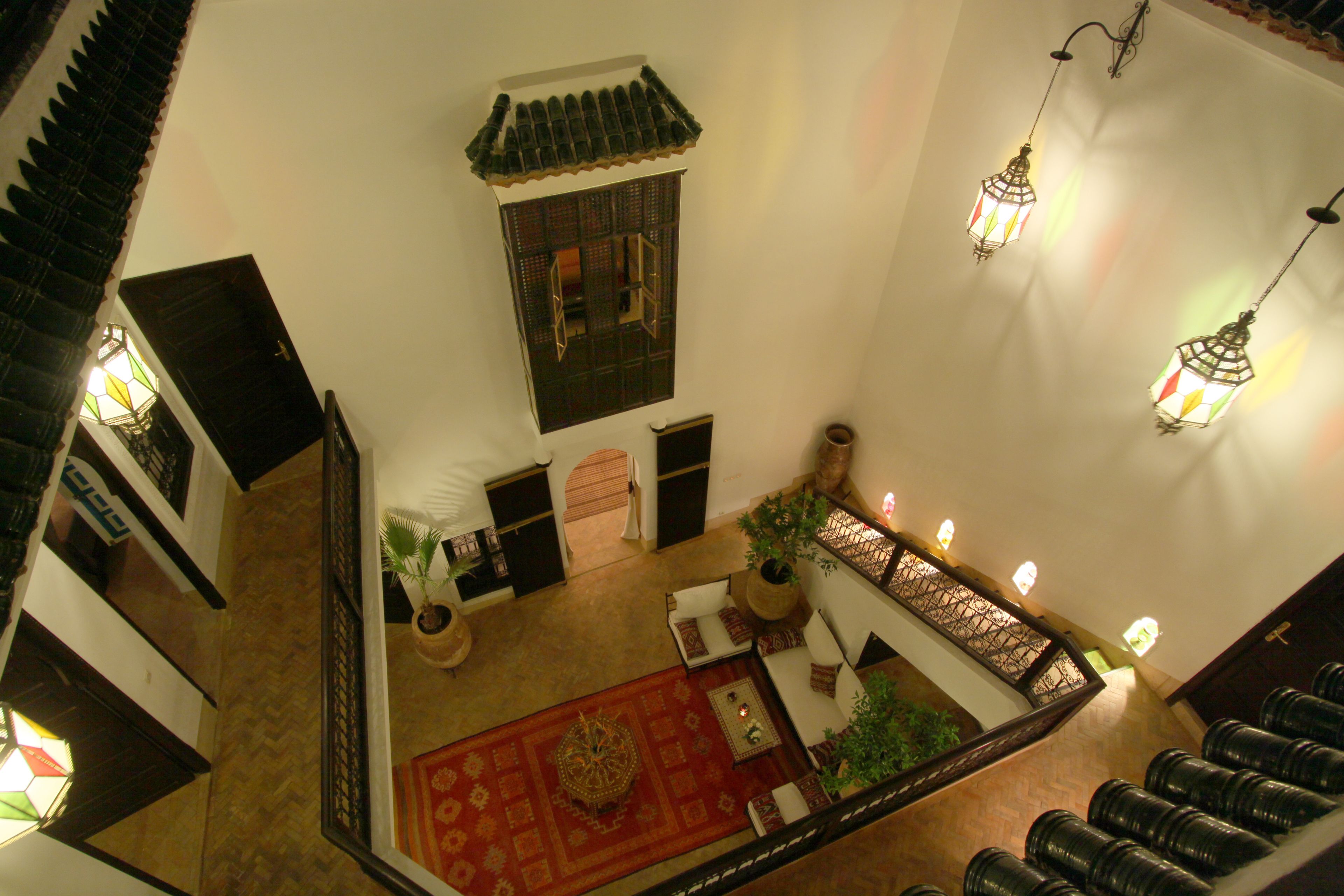 Un intérieur traditionnel avec un tapis rouge à motifs, un escalier en bois et un coin salon agrémenté de coussins.