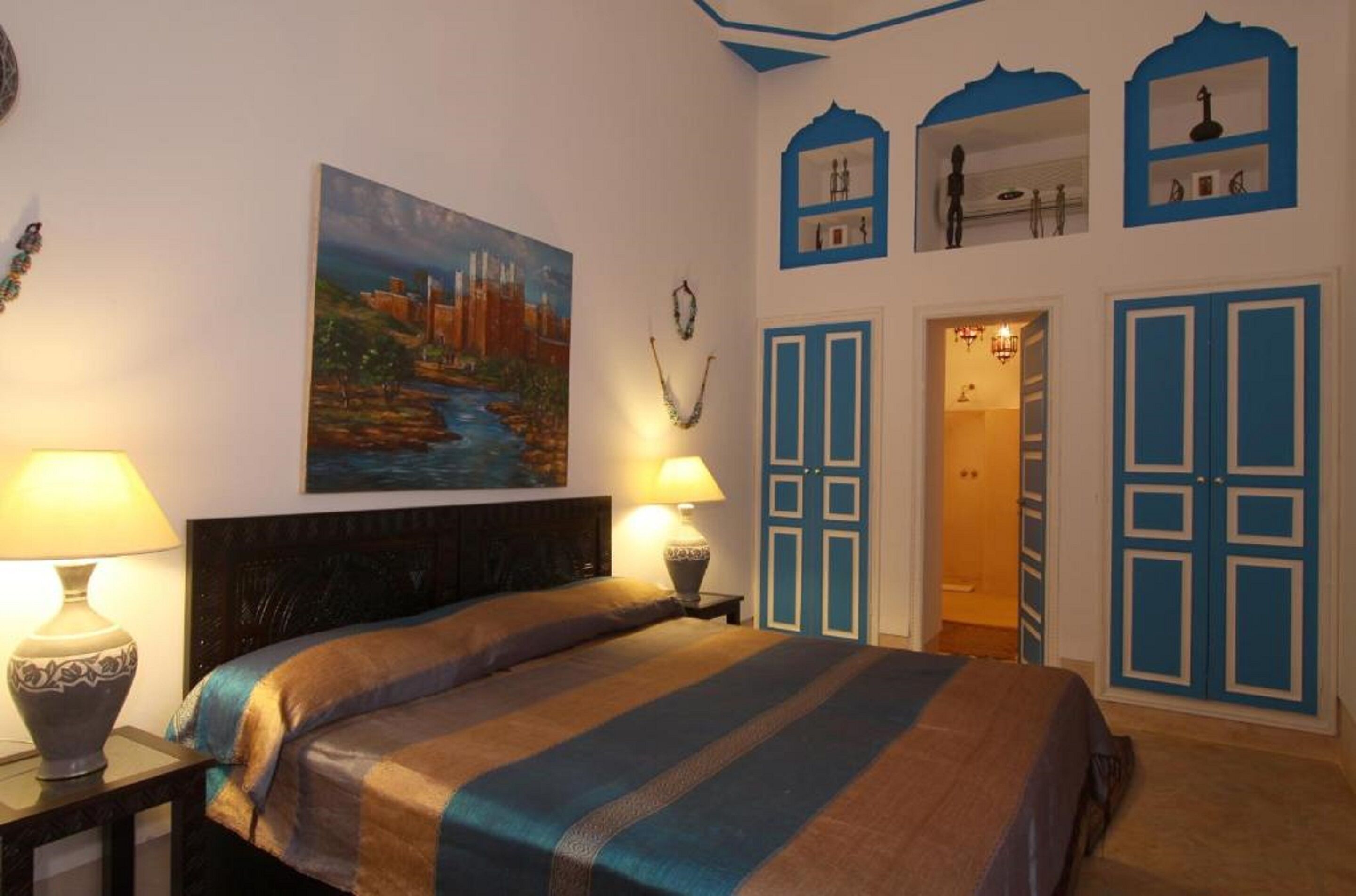 A bedroom with a bed, two bedside lamps, a painting on the wall, and blue doors.