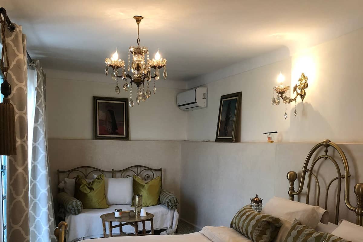 Un dormitorio con una cama grande, una araña, una mesita de noche y aire acondicionado instalado en la pared.