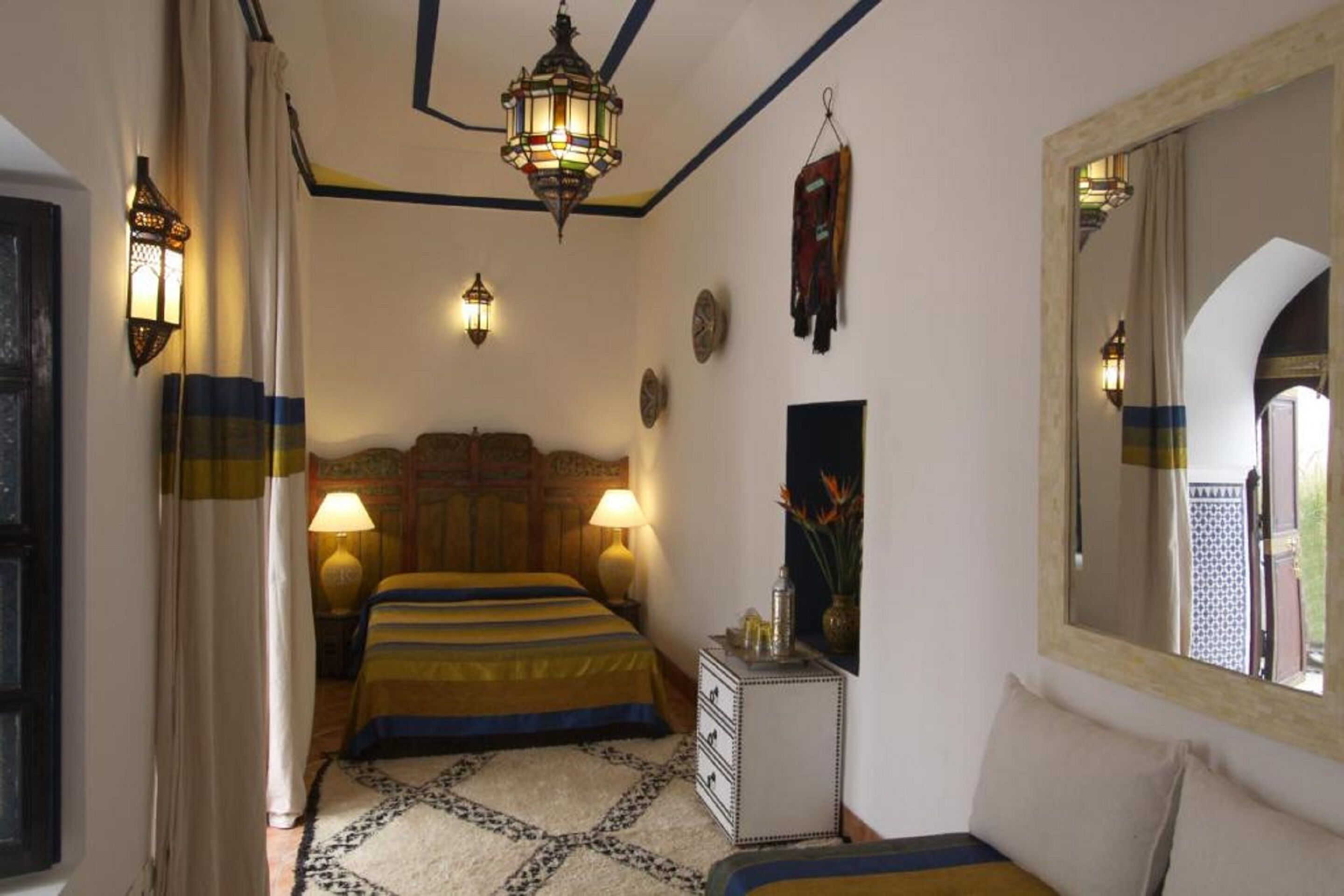 A bedroom with a bed, two wall-mounted lamps, a mirror, and a small table with a vase.