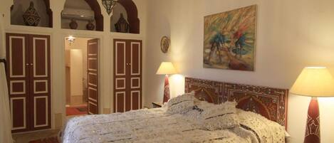 A bedroom with a large bed, two bedside lamps, a chandelier, and a painting on the wall.