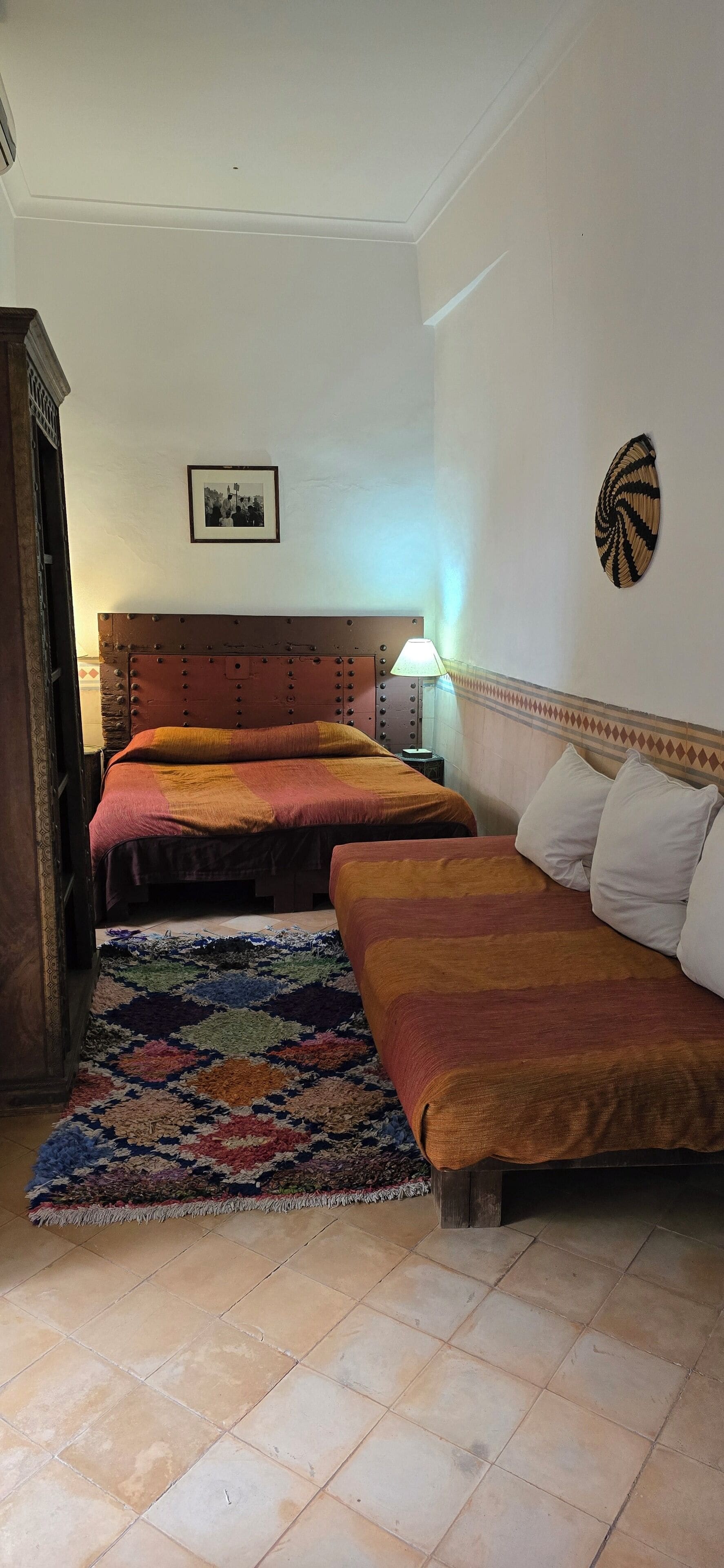 Une chambre avec deux lits, un tapis à motifs, une lampe fixée au mur et un élément décoratif mural.
