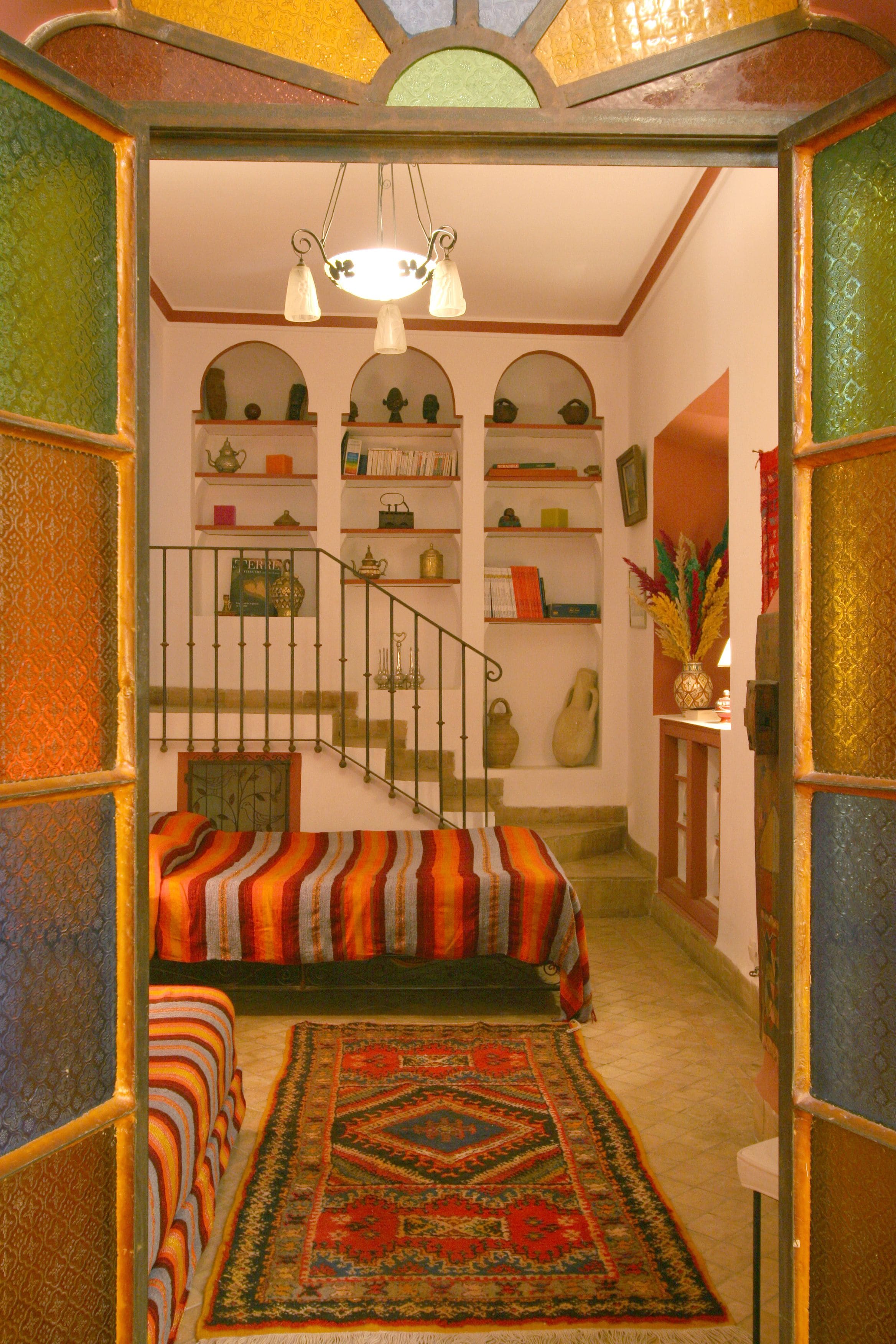 Una escalera conduce a un dormitorio con una colcha a rayas de colores y una alfombra estampada.