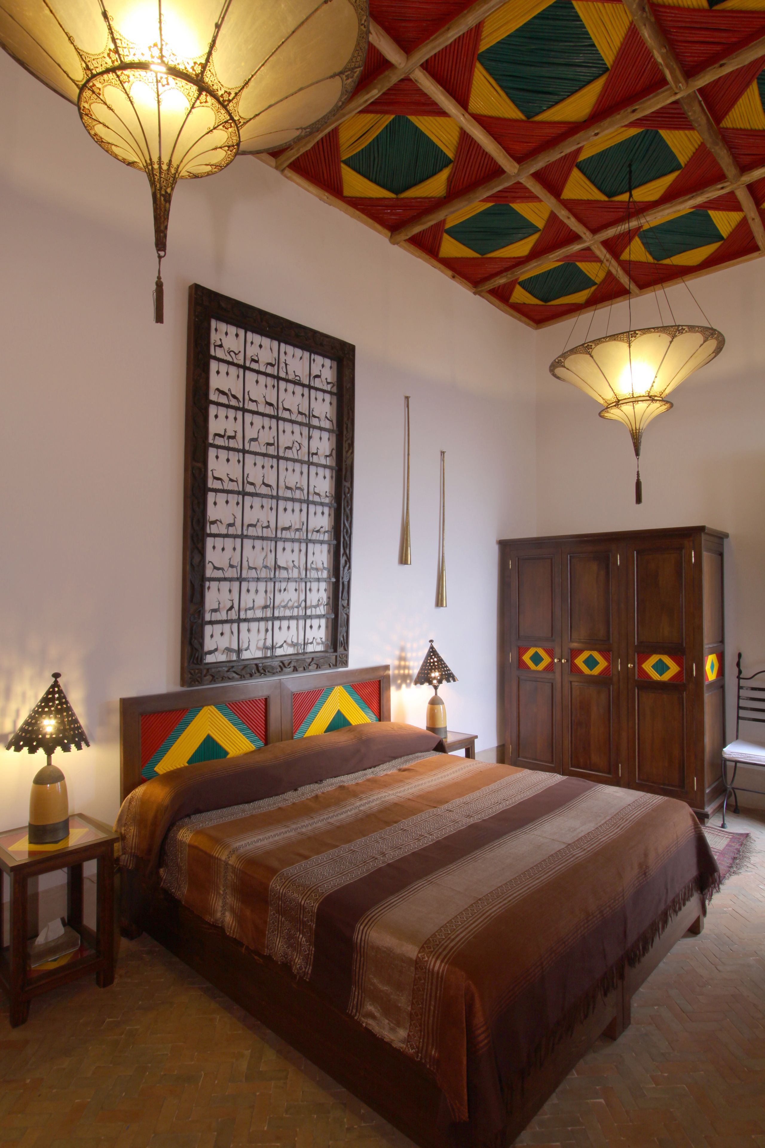 A bedroom with a large bed, a wooden wardrobe, a decorative ceiling, and a wall-mounted artwork.