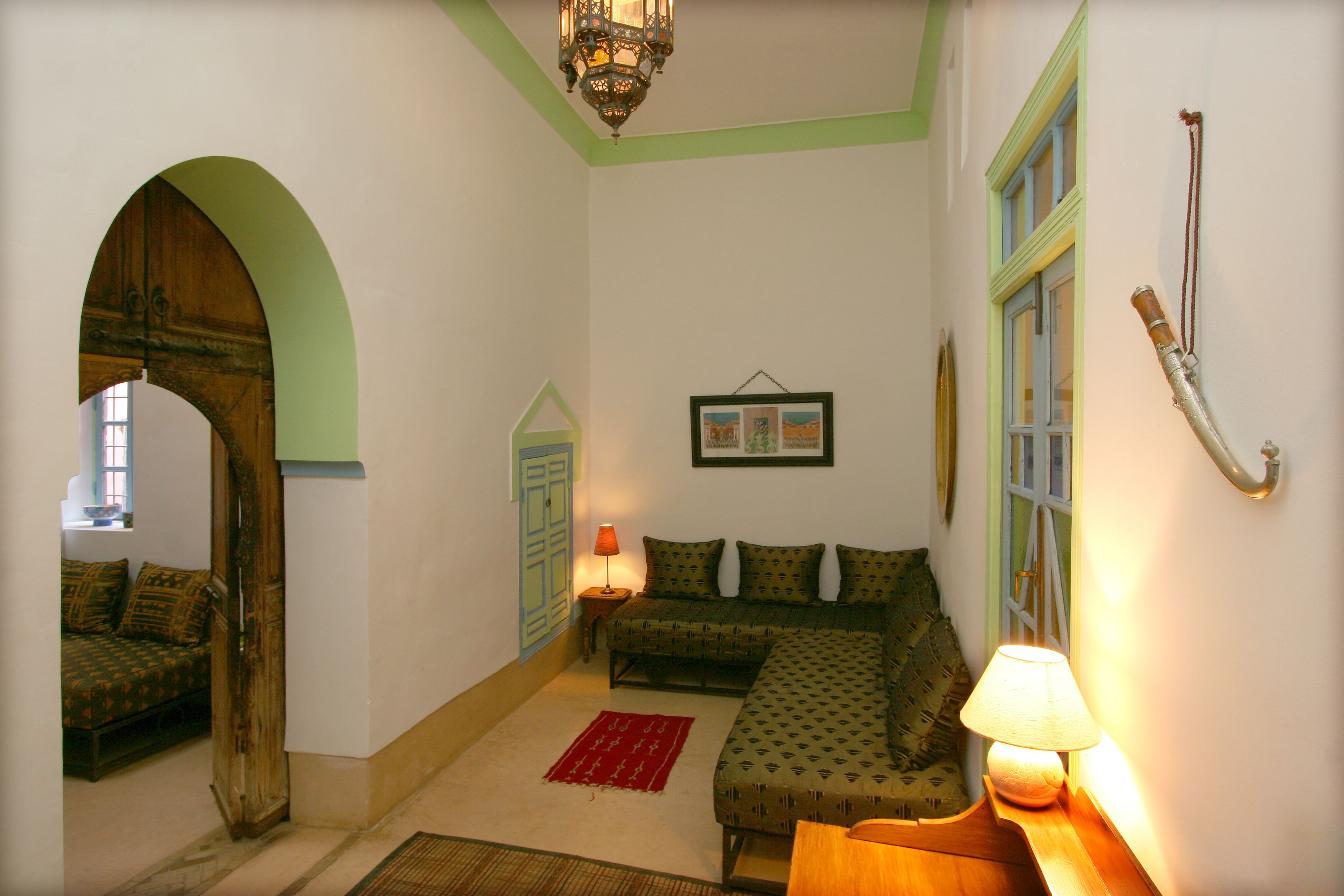 A cozy room with a wooden door, a sofa, a red rug, and a lamp.
