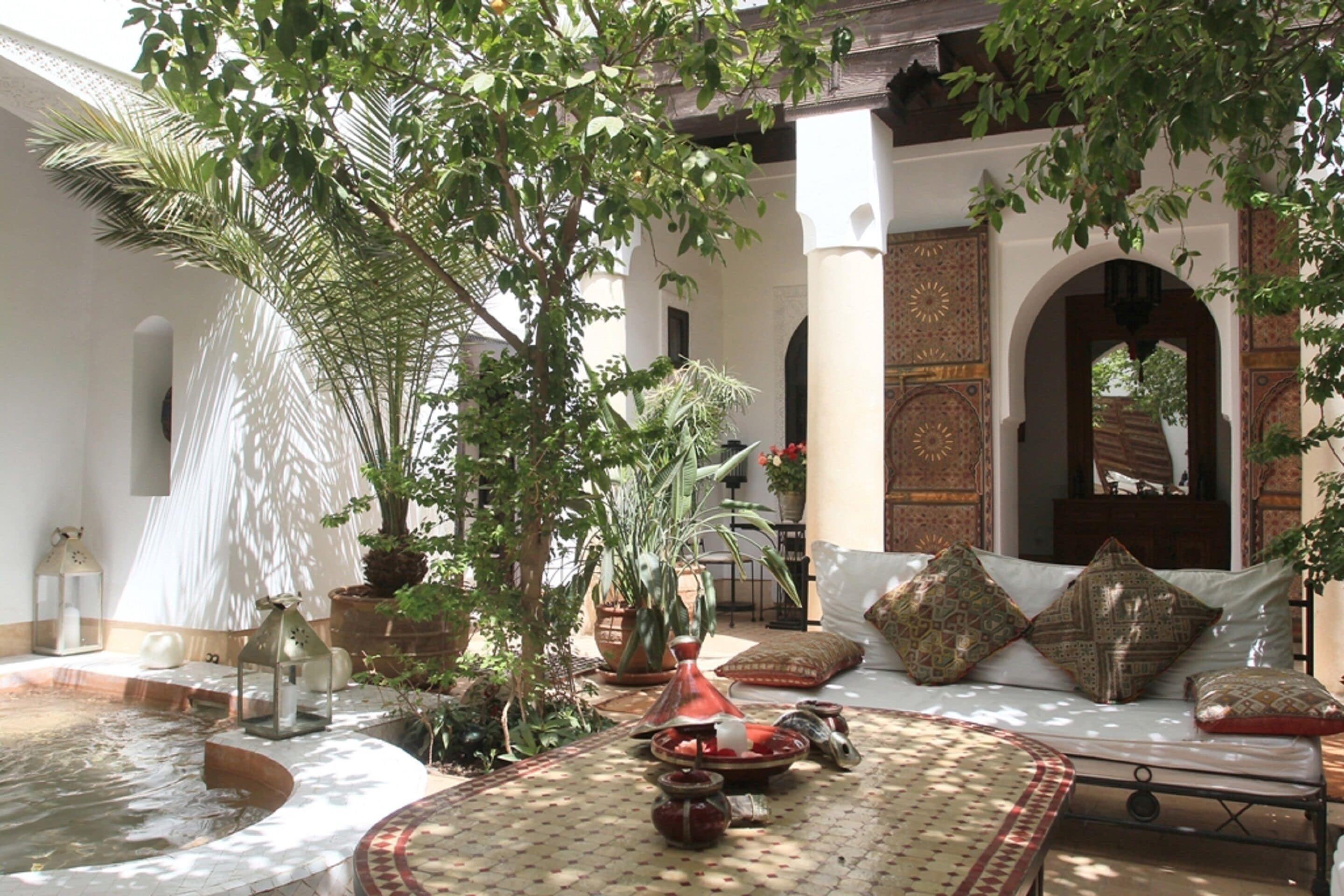 A traditional Moroccan interior with a seating area, a fountain, and potted plants.
