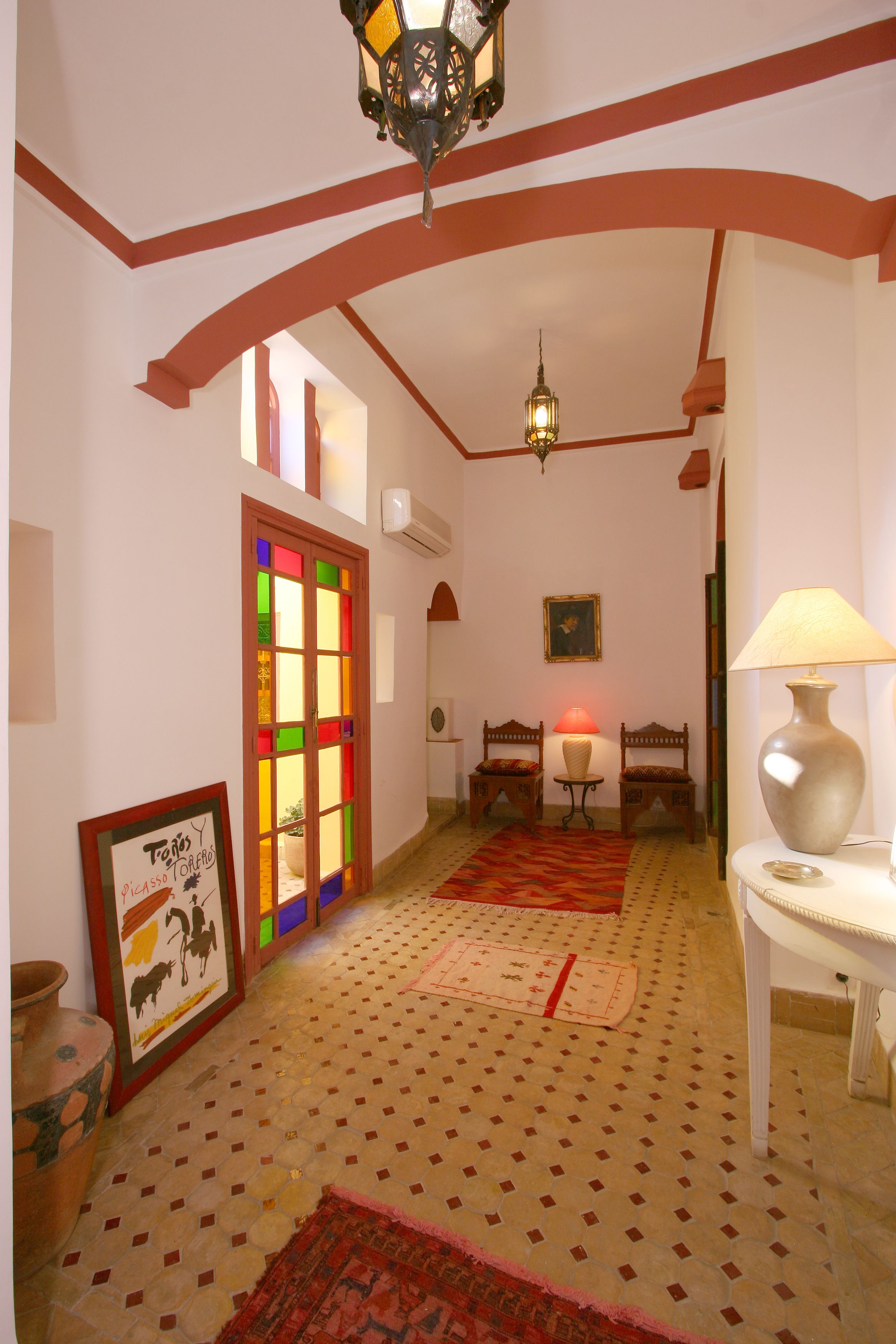 Un couloir doté d’un sol à motifs, d’une porte en vitrail aux couleurs vives et d’une lampe de style traditionnel.