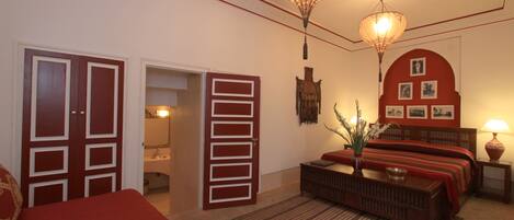 A hotel room with a bed, a nightstand, a lamp, a wall-mounted shelf, and a door.