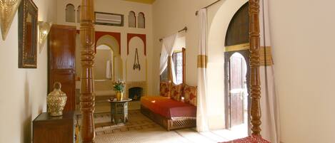 A bedroom with a four-poster bed, a small table with a vase, and a sofa.
