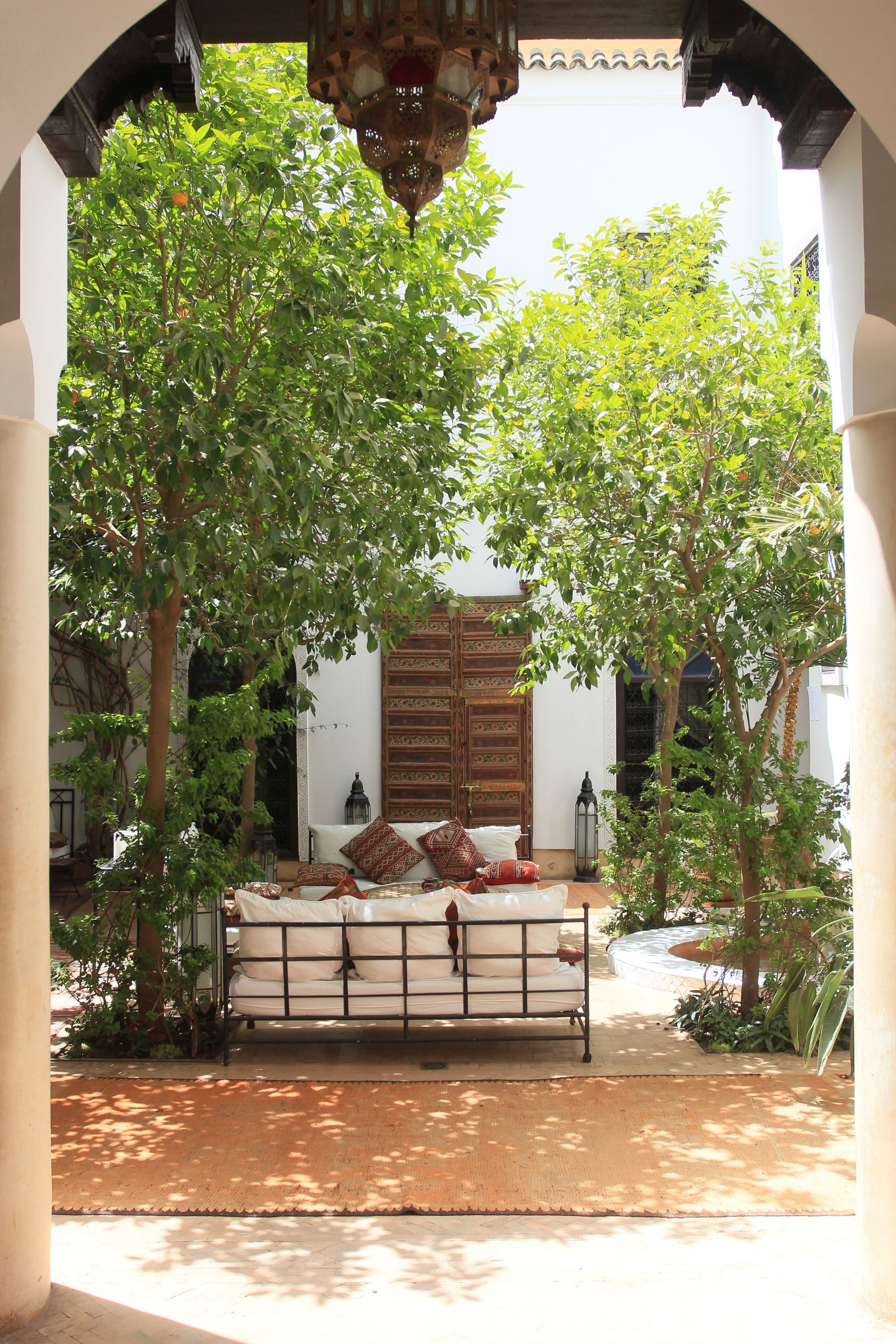 A courtyard with a bed, a wooden door, and a hanging lantern.
