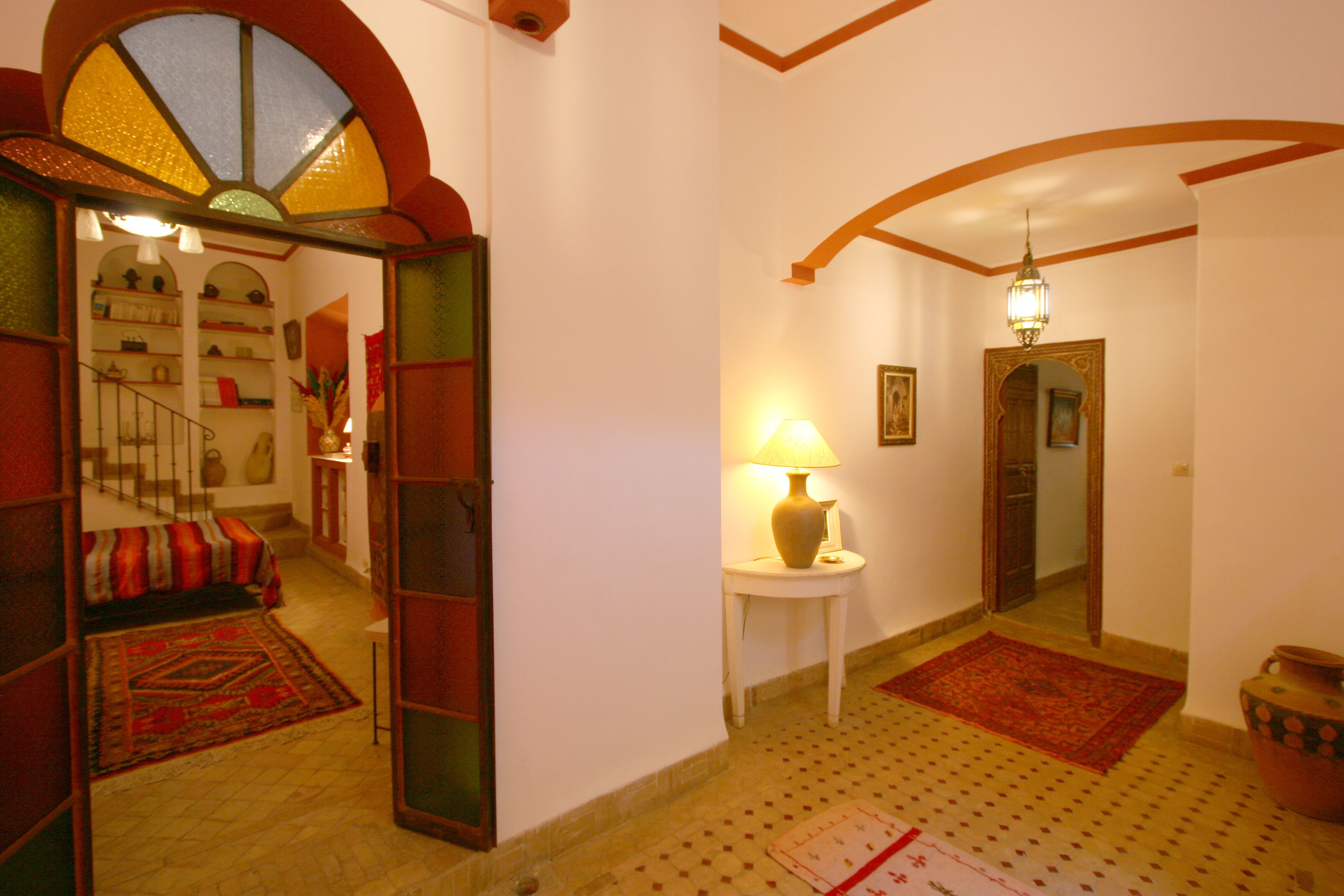 A hallway with a staircase, a lamp, and a rug.