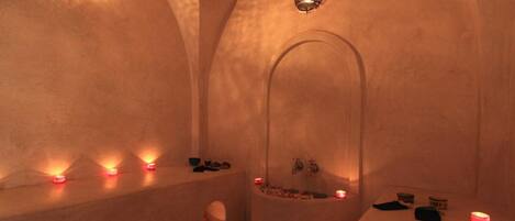 A dimly lit spa room with a large bathtub, candles, and a shelf with toiletries.