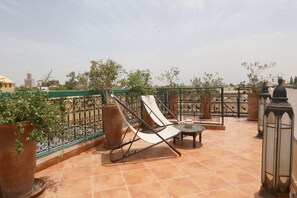 A rooftop terrace with a lounge chair, potted plants, a small table, and a lantern.