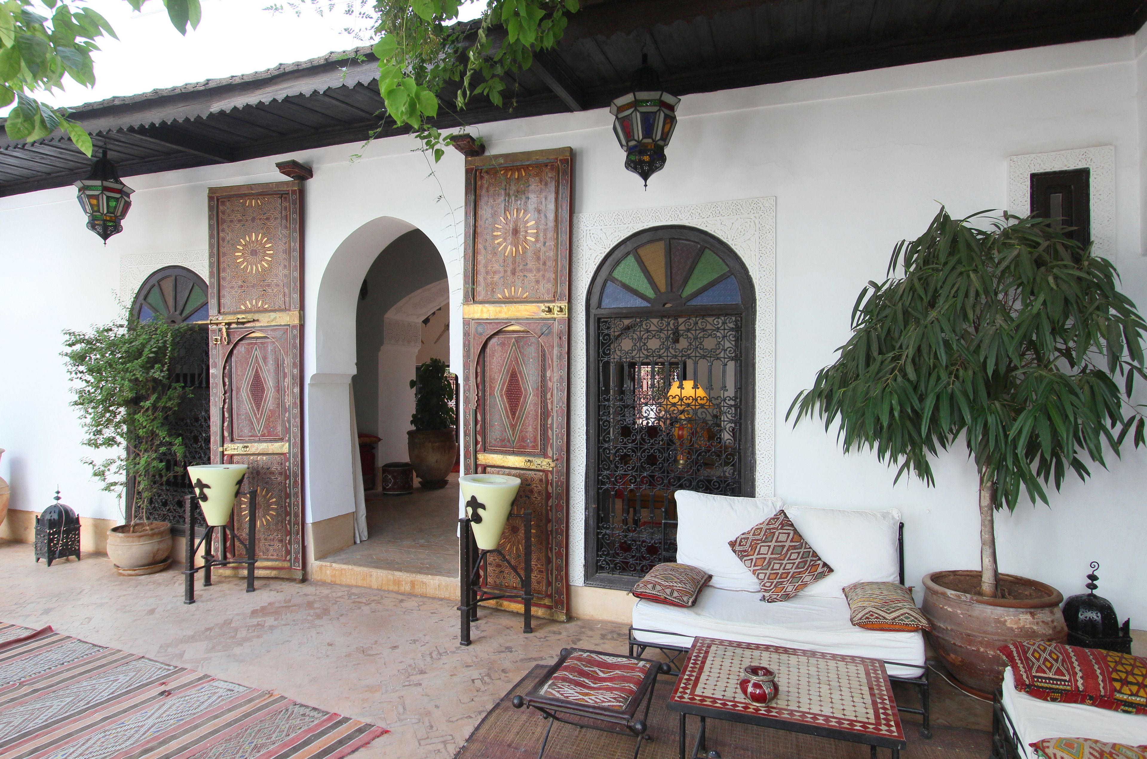 Un patio tradicional con un sofá, sillas y una mesa. Hay plantas en macetas y un árbol grande.