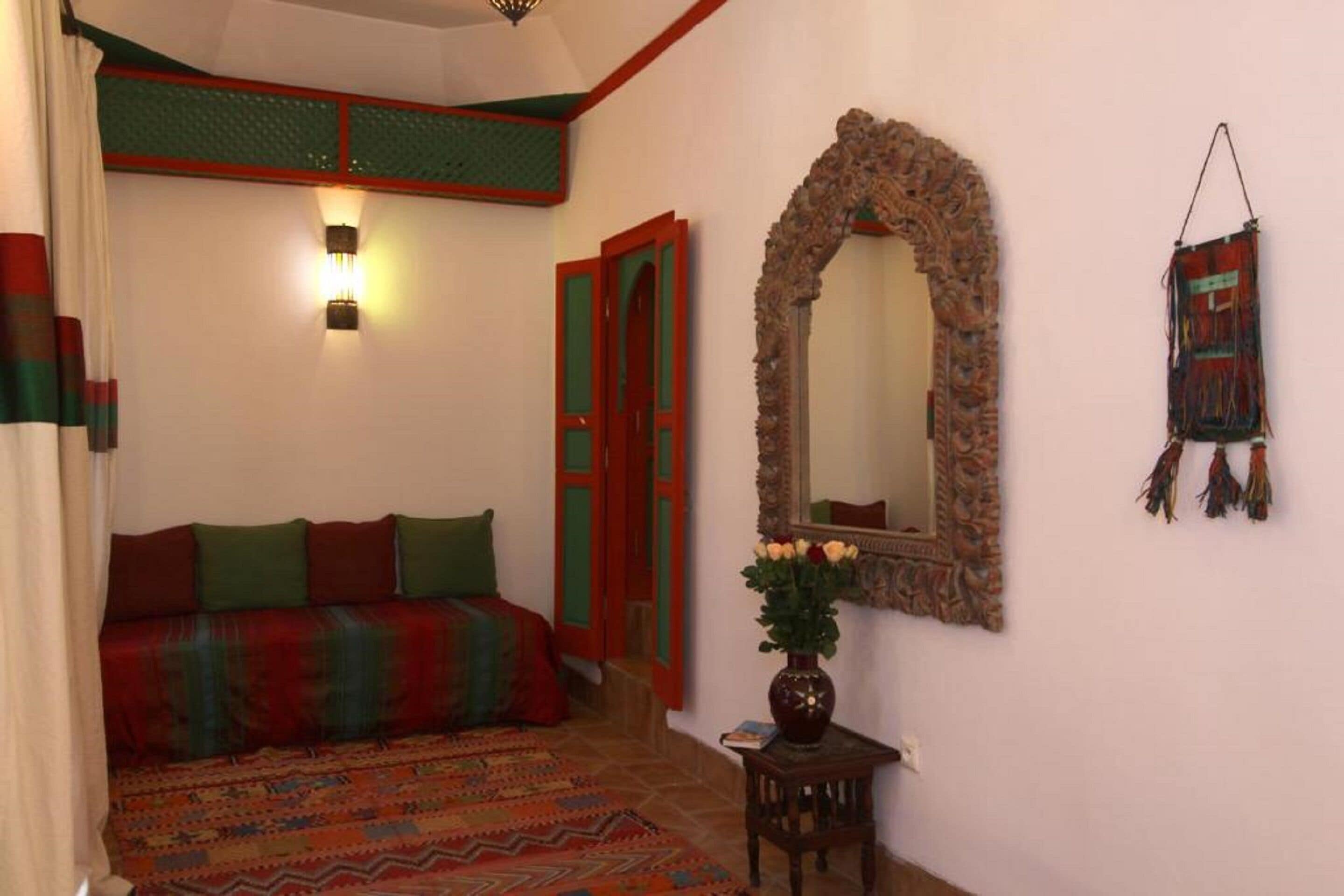 A bedroom with a bed, a mirror, a wall-mounted light, and a door.