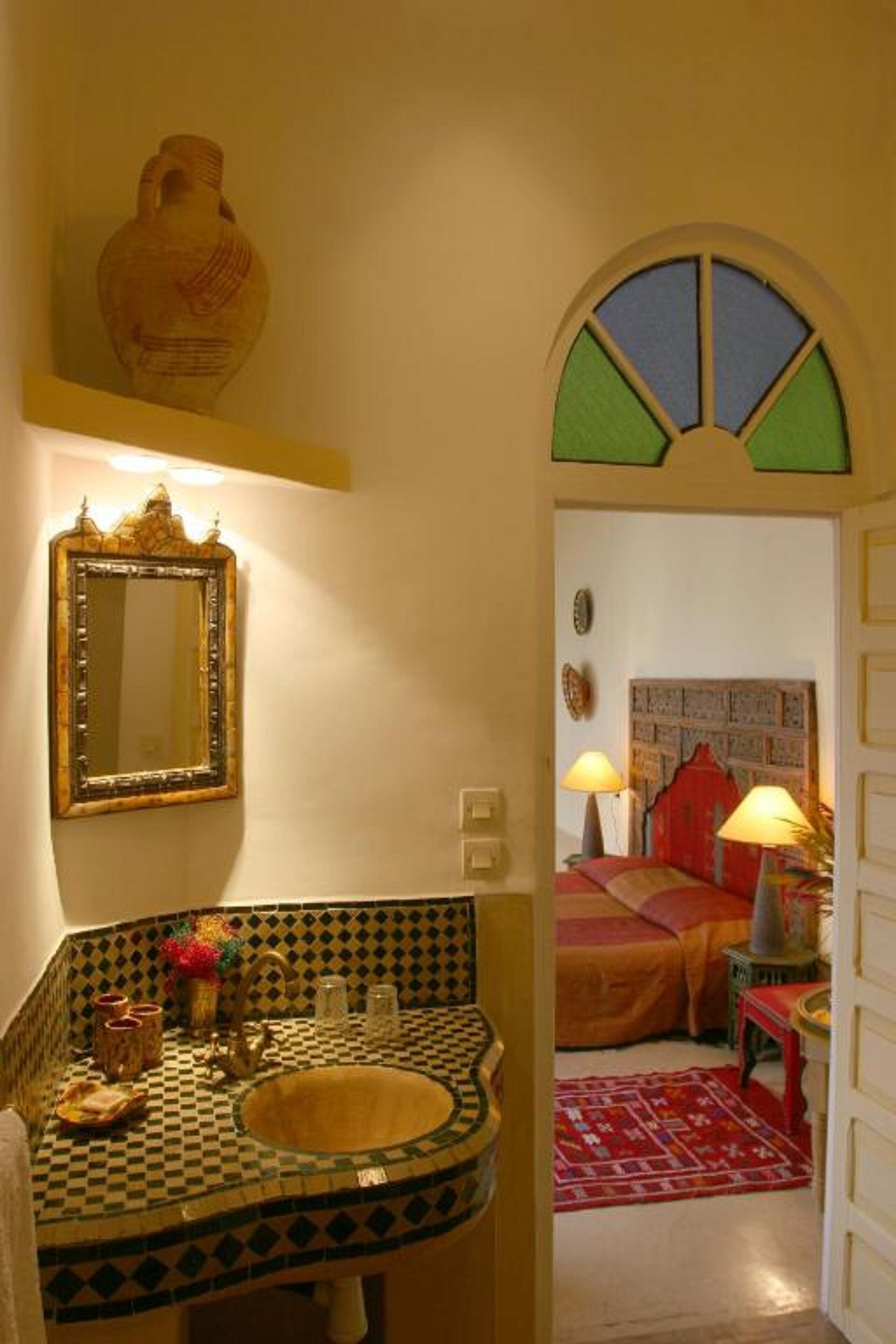Un baño con lavabo de baldosas a cuadros, un espejo y un jarrón decorativo.
