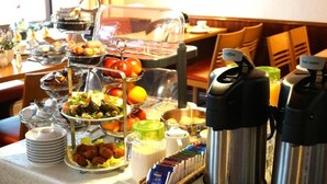 Ein reichhaltiges Buffet mit verschiedenen Speisen, darunter Salate, Früchte und Fleisch, sowie Kaffee- und Warmwasserautomaten.