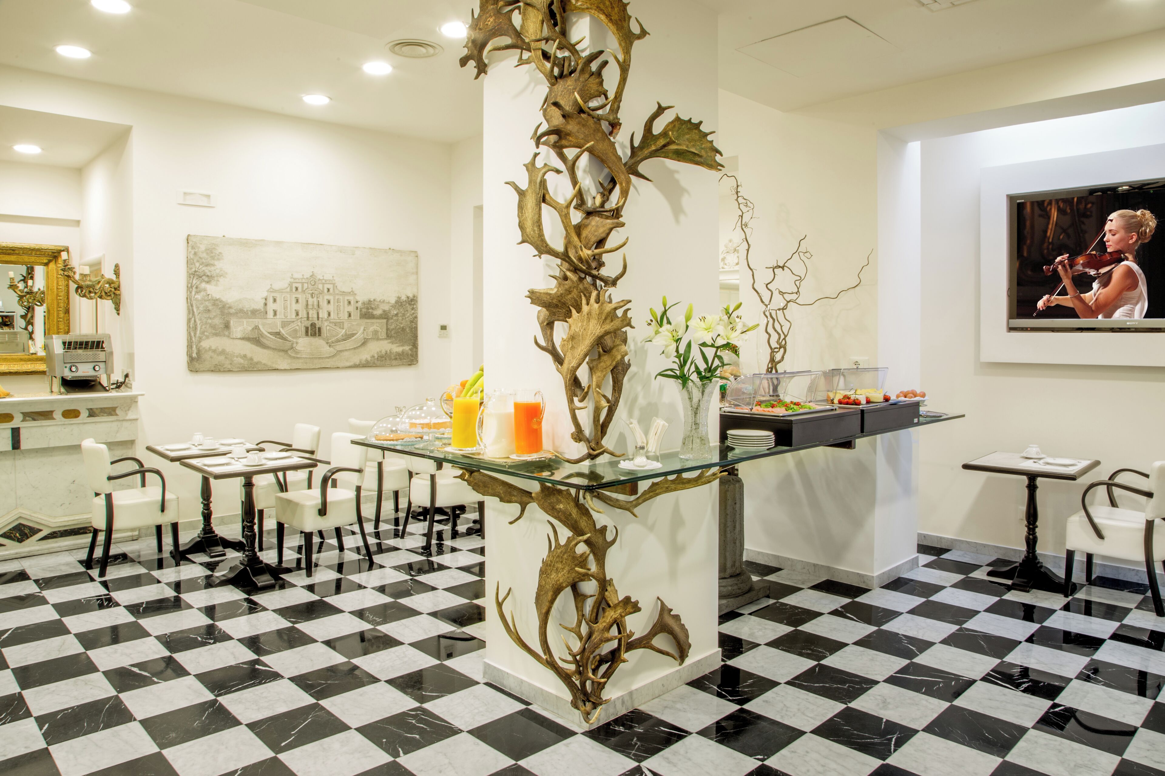 A dining area with a checkered floor, a central glass table with a decorative metal pillar, white chairs, and a painting on the wall.