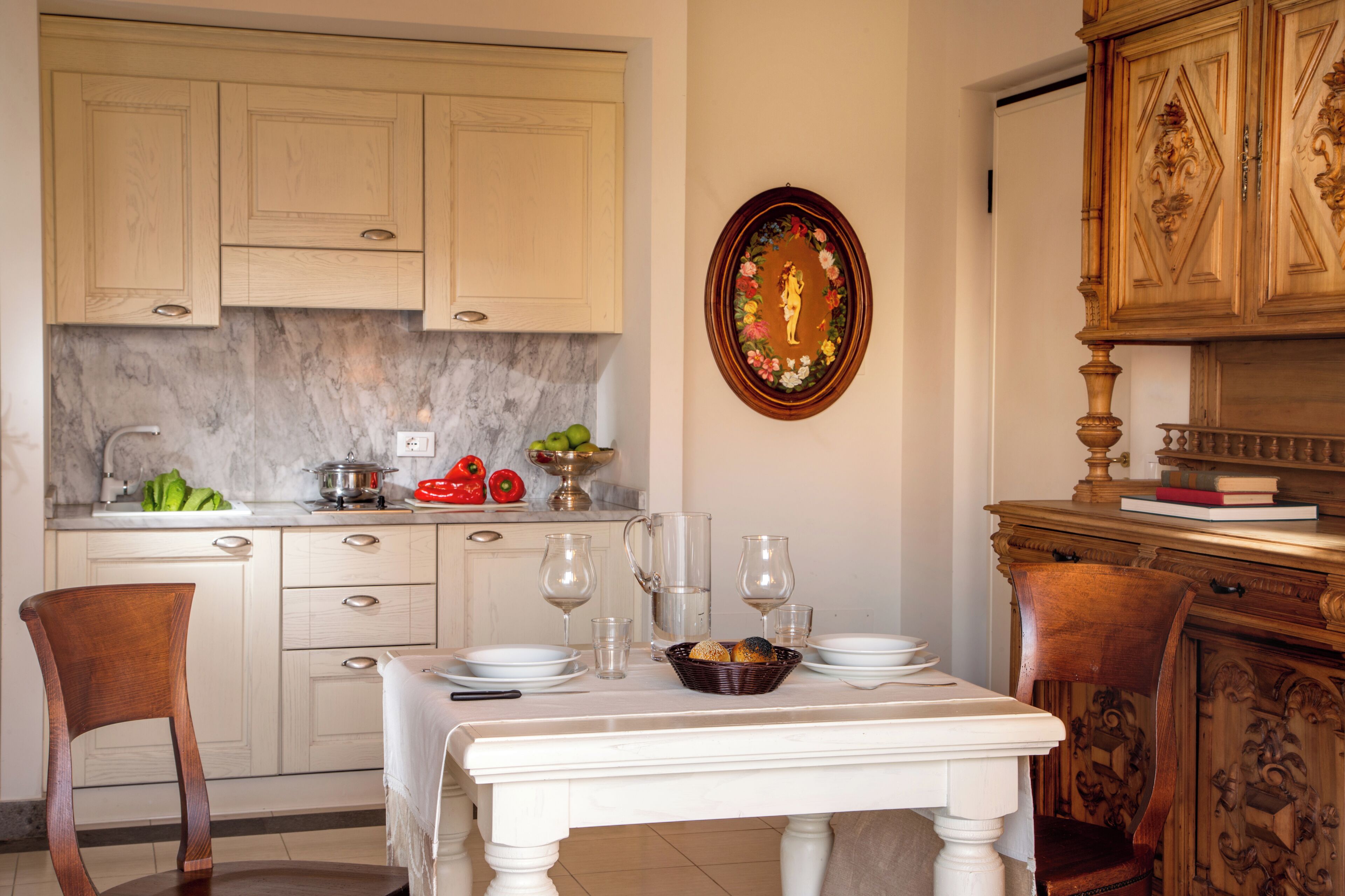 Un coin repas avec une table dressée pour deux personnes, une cuisine en arrière-plan et un élément décoratif mural.