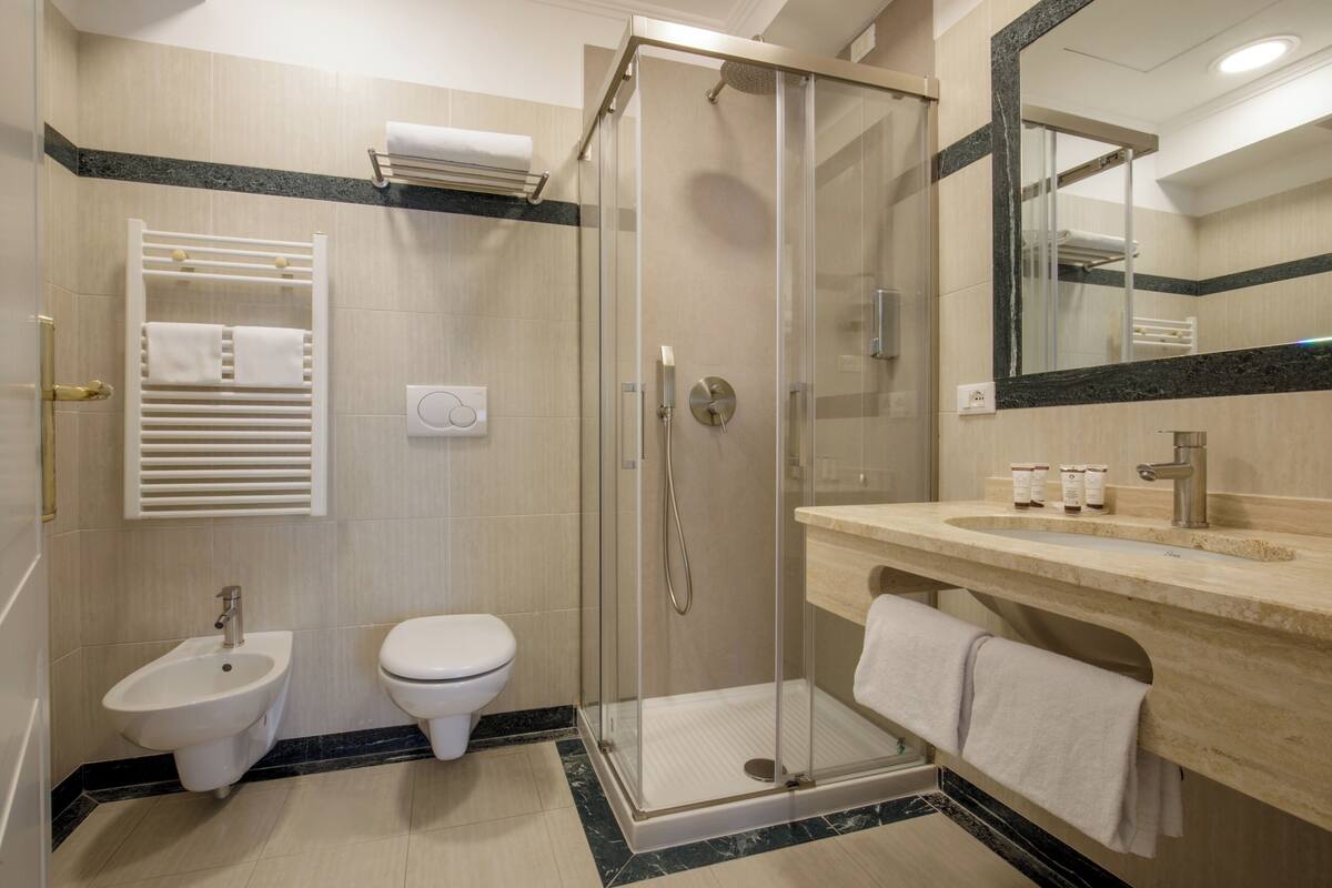 A modern bathroom with a glass shower enclosure, a bidet, a toilet, and a vanity with a mirror.