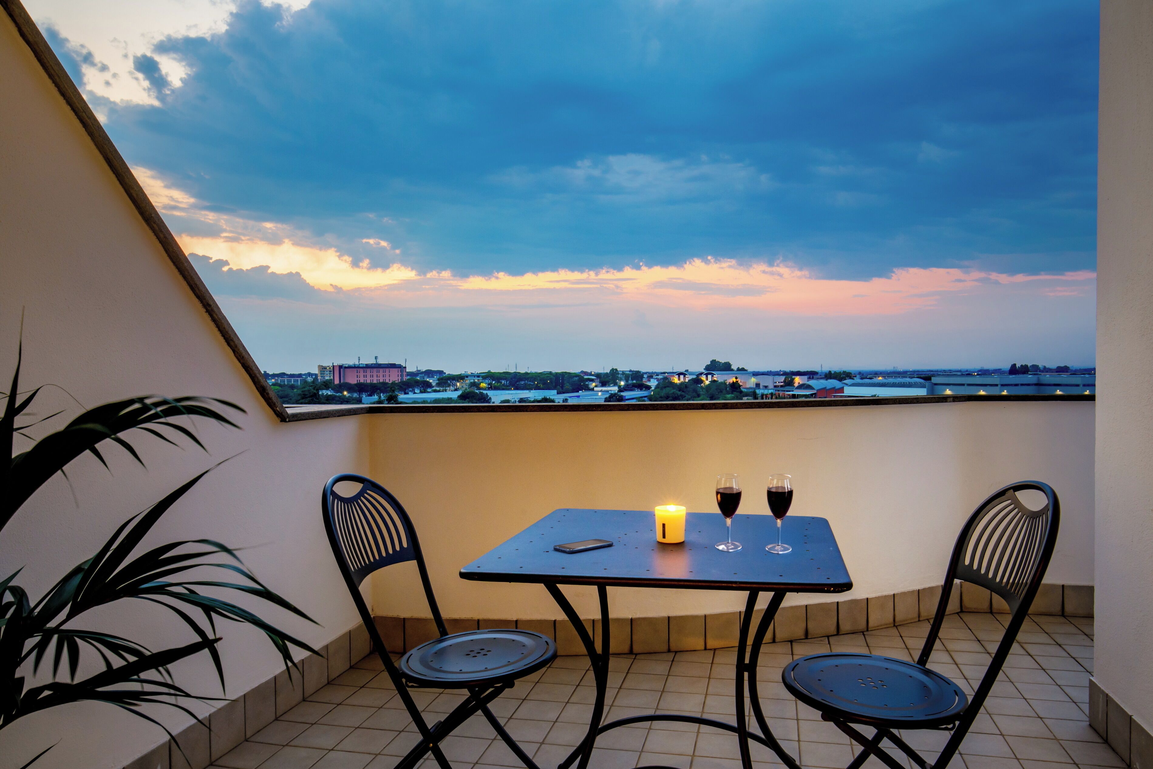 Ein Balkon mit Tisch, Stühlen, einer Kerze und einem Weinglas.