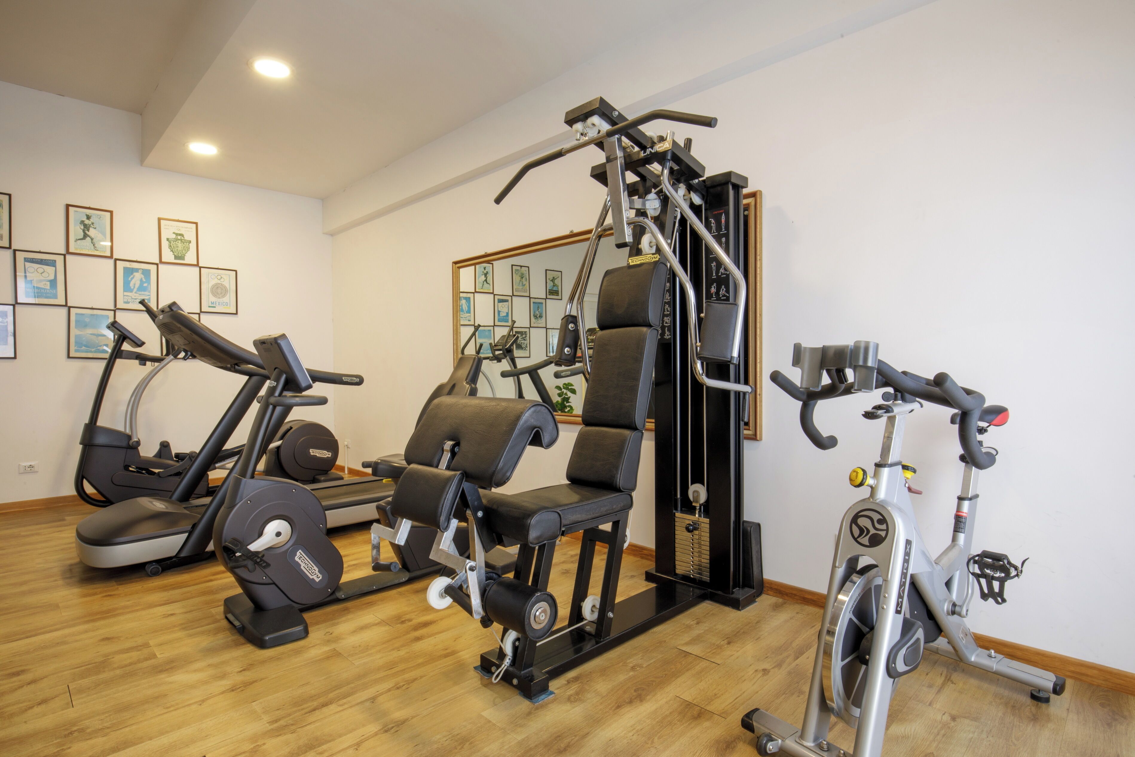 A gym with exercise equipment, wooden flooring, and framed pictures on the walls.