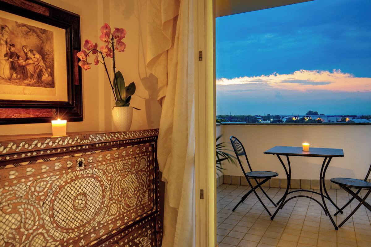 A balcony with a table and chairs, a candle, a framed picture, and a potted orchid.