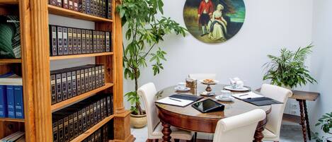 A dining area with a round table, chairs, a bookshelf, and a painting on the wall.