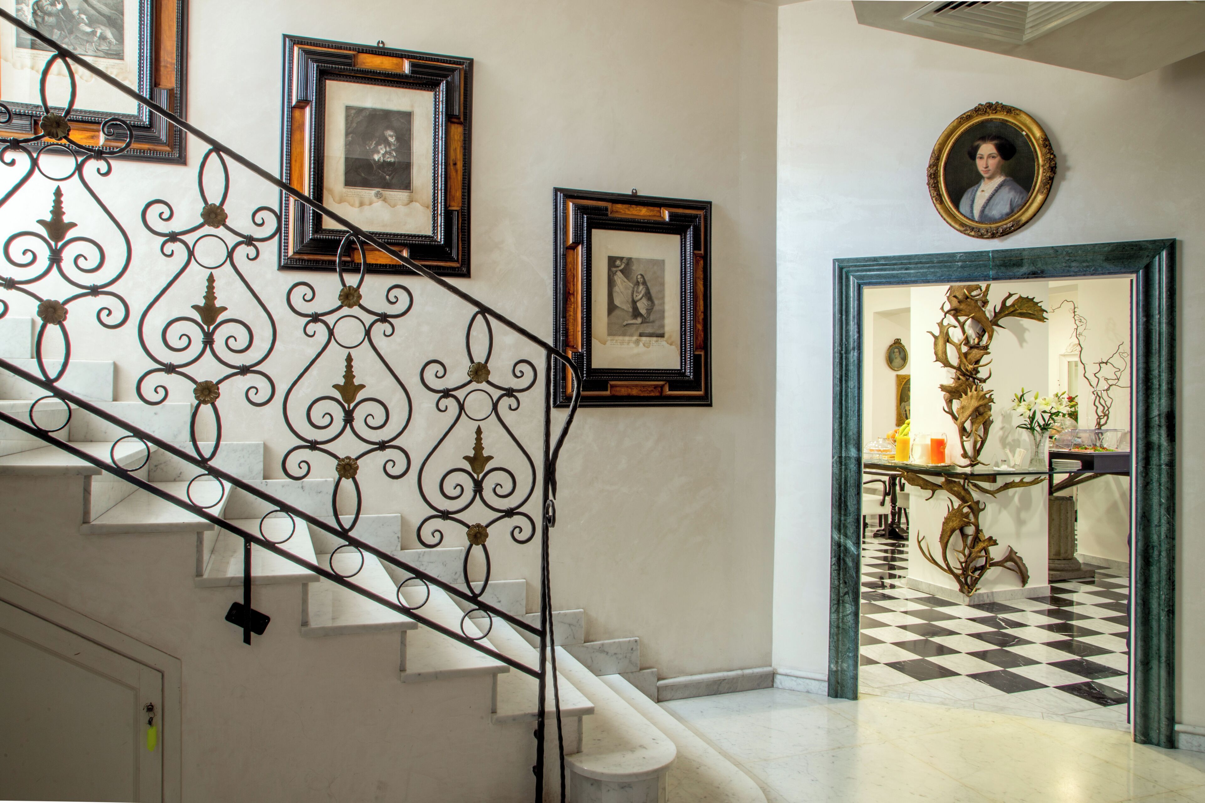 Eine Treppe mit aufwendigen Metallgeländern, einem Schachbrettmuster im Boden und gerahmten Kunstwerken an den Wänden.
