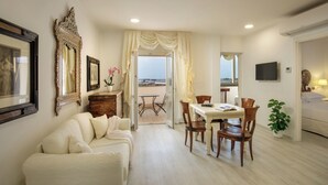 A hotel room with a dining area, a sofa, a television, and a view of the sea. - Arcom Palace (Pomezia)