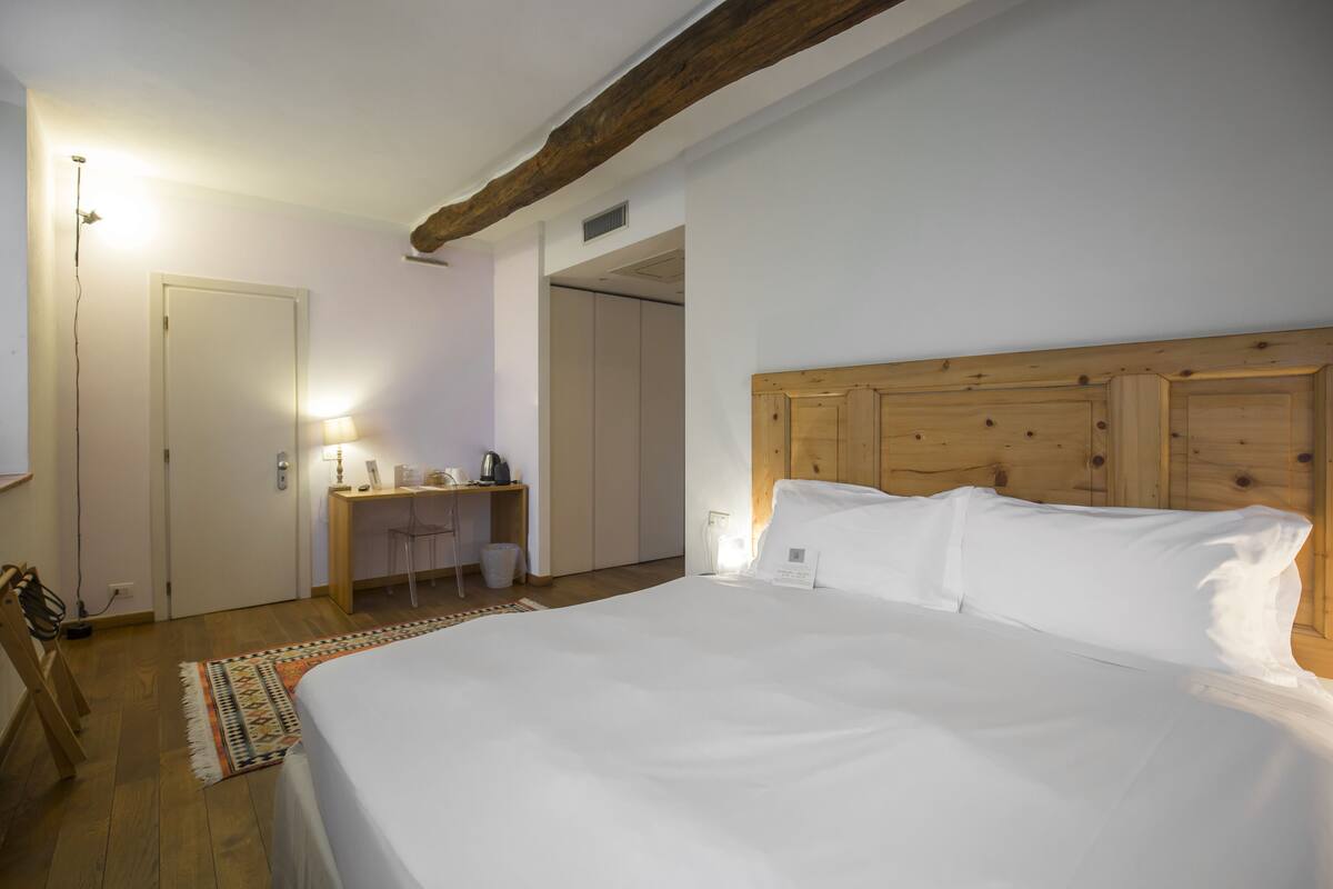 A bedroom with a large bed, a wooden headboard, a desk with a chair, and a small rug.