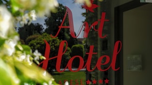Un letrero de hotel con el texto 'Art Hotel' y una vista parcial de un jardín con follaje y flores.