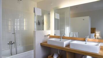 A bathroom with two sinks, a bathtub, and a shower. There are wicker baskets under the sinks and a patterned rug on the floor.